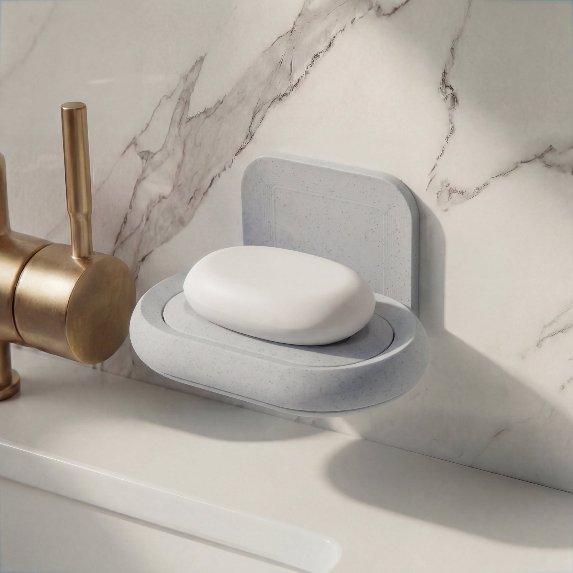 Gray soap holder with a bar of soap on a marble countertop next to a brass faucet.