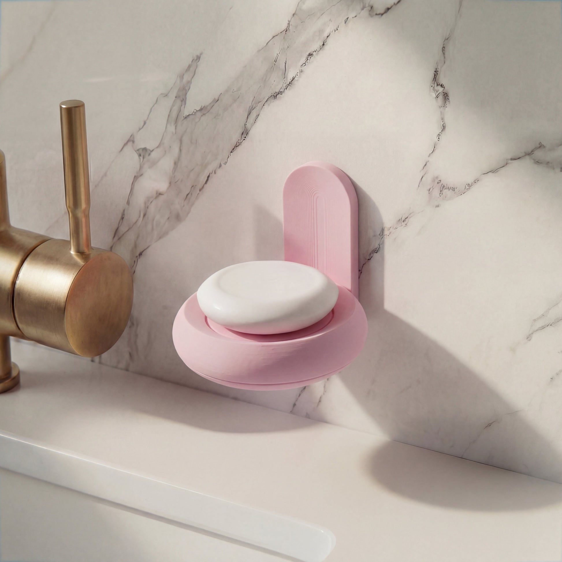 Pink soap holder with a bar of soap over a marble countertop next to a brass faucet.