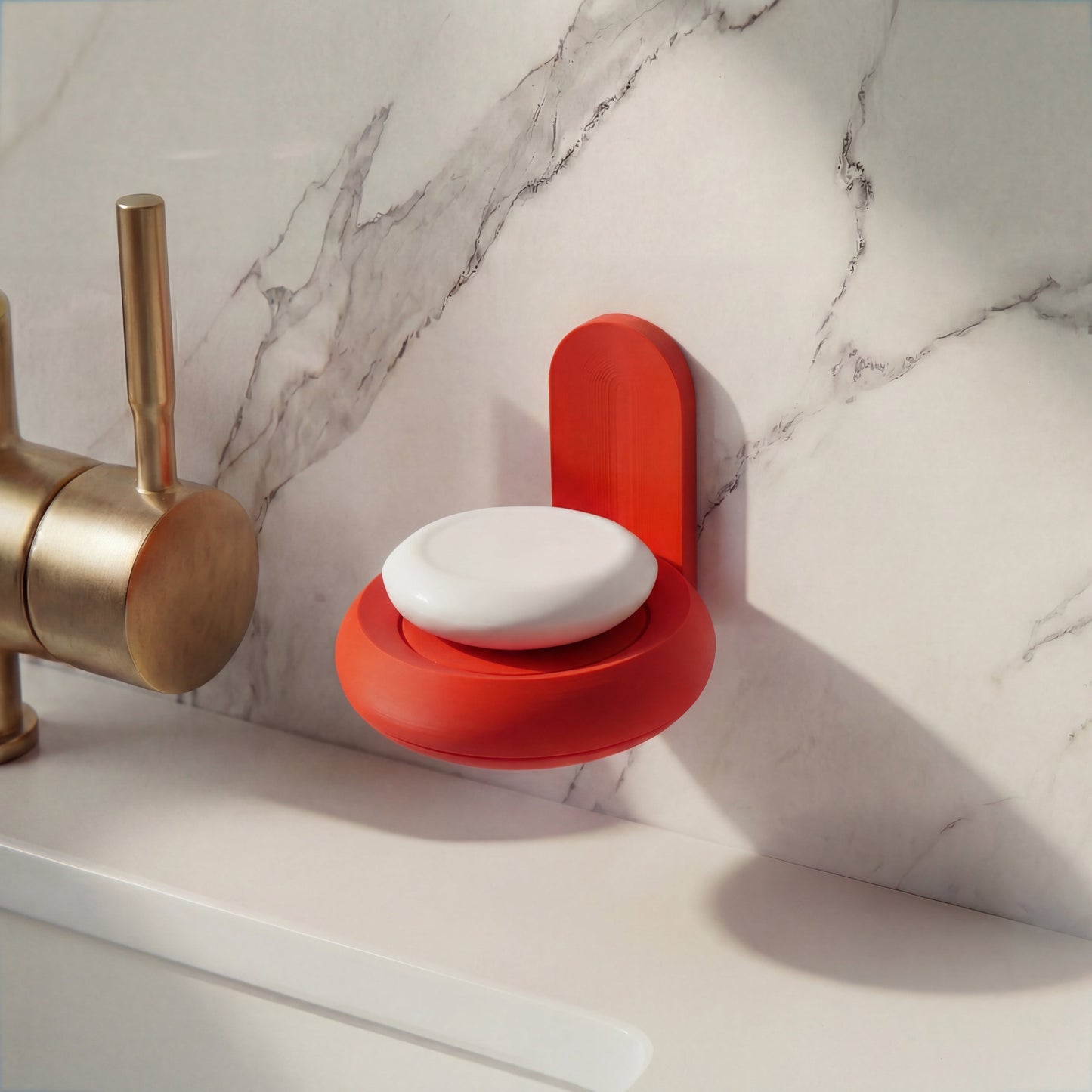 Red soap holder with a bar of soap on a marble countertop next to a brass faucet.