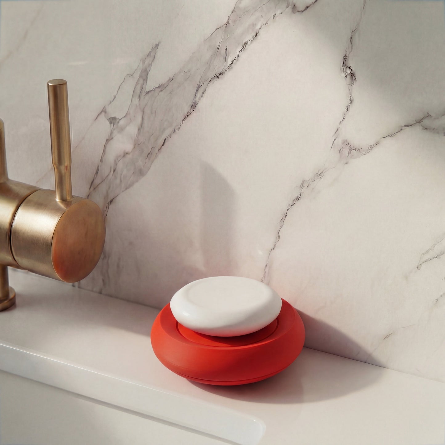 Red soap dish on a marble bathroom counter with a brass faucet.