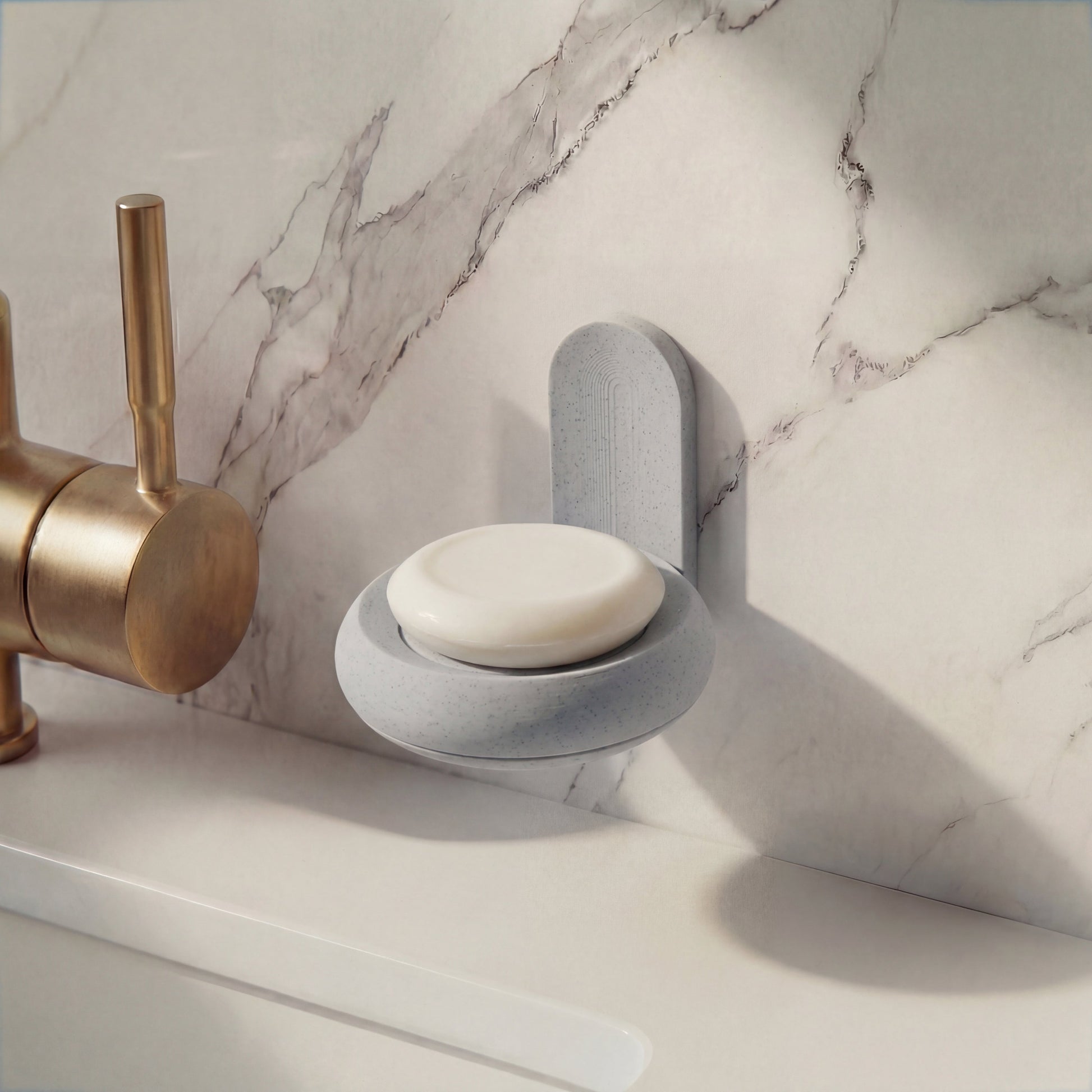 Gray soap holder with a bar of soap over a marble countertop with a brass faucet.